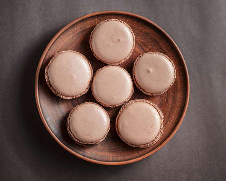Chocolate pastel brown Macarons or Macaroons on a plate over dark background