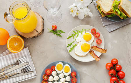 Breakfast table with fried eggs, bacon, cherry tomatoes, sandwichesの写真素材