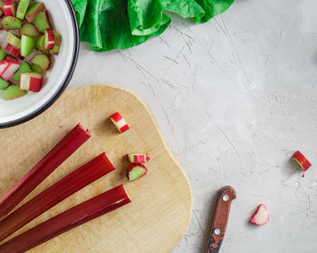 Fresh organic rhubarb stems on wooden cutting board over grey concrete stone backgroundの写真素材