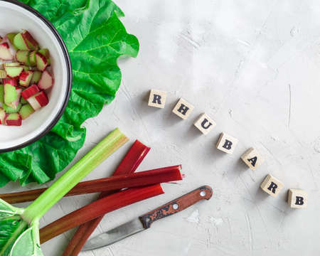 Fresh organic rhubarb stems with cut pieces in metal bowl over grey concrete stone background. Word Rhubarb written with wooden blocks lettersの写真素材