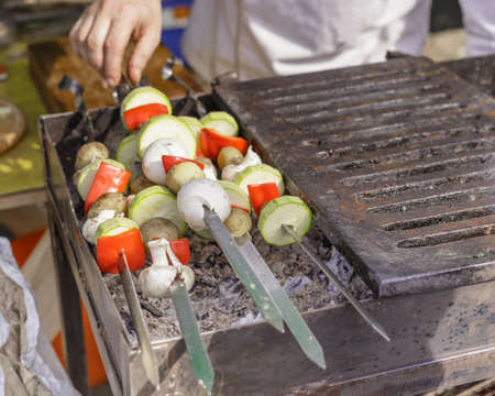 Vegetables and mushrooms grilling with metal skewers at street food marketの写真素材