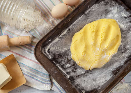 Raw dough for pie in baking pan with ingredients on the table. Cooking process