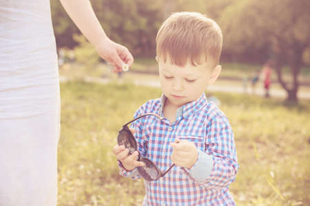 Toddler boy playing with his mother's sunglasses while walking with her in the parkの写真素材