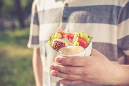 Man is holding falafel sandwich in paper bag. Healthy street food concept, oriental cuisine. Selective focus on foodの写真素材