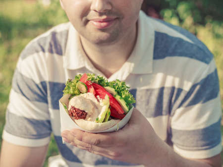 Man is holding falafel sandwich in paper bag. Healthy street food concept, oriental cuisine. Selective focus on foodの写真素材