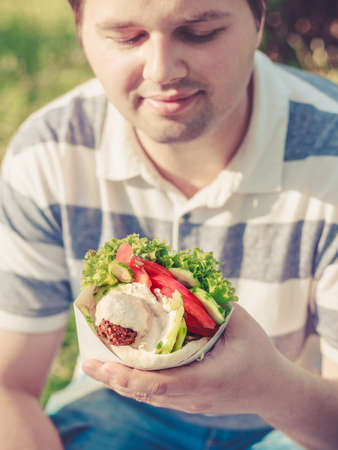 Man is holding falafel sandwich in paper bag. Healthy street food concept, oriental cuisine. Selective focus on foodの写真素材