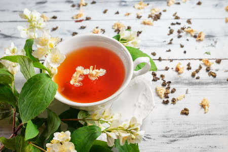 White porcelain cup of tea with jasmine flowers on a white wooden table. Selective focus on top of the cupの写真素材