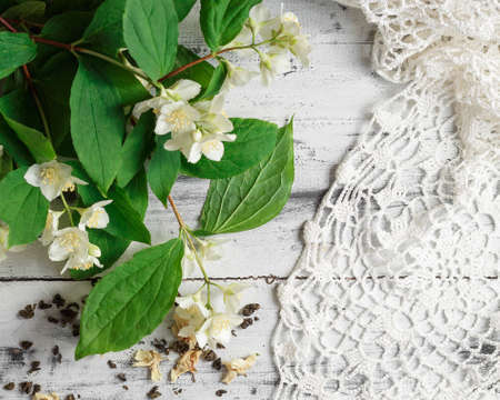Scattered dried green tea leaves with fresh jasmine flowers and crochet doily on a white wooden table. Top viewの写真素材