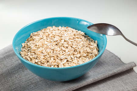 Oat flakes in blue ceramic bowl ready to cook and spoon on the white table with grey clothの写真素材
