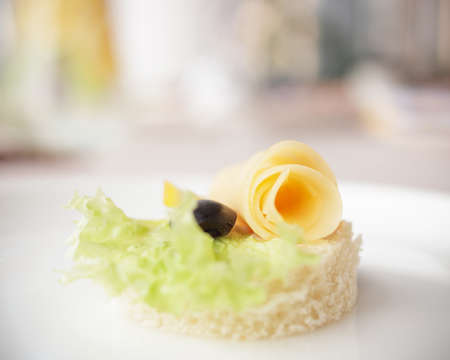 Canape with cheese, lettuce and black olive on white plate. Festive appetizer close up. Selective...