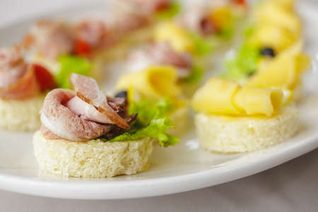 Canape set with ham, cheese, lettuce and black olive on white plate. Festive appetizer close up....