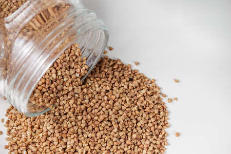Uncooked buckwheat scattered from glass jar on the kitchen table. Selective focusの写真素材
