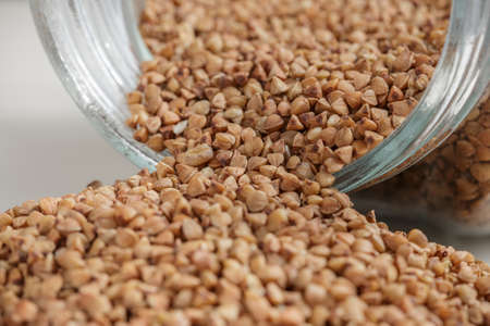 Uncooked buckwheat scattered from glass jar on the kitchen table. Selective focusの写真素材