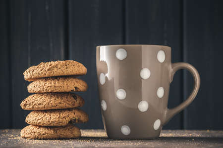Stack of oat cookies and polka dot mug with hot drink over dark wooden backgroundの写真素材