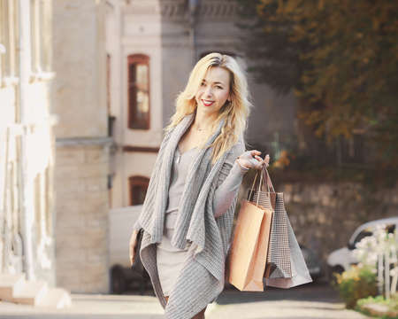 Young stylish woman carrying shopping bags while walking on the old city street in autumn. Casual fashion, elegant lookの写真素材