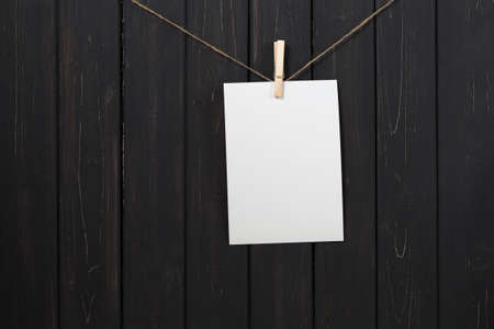 Blank white paper card hanging attach to rope with clothes pins on black wooden backgroundの写真素材