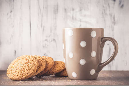 Oat cookies and polka dot mug with hot drink over wooden backgroundの写真素材