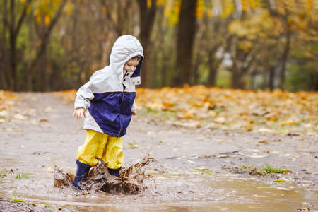 Happy two years old boy jumping on muddy puddles in rubber bootsの写真素材