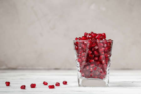A glass filled with pomegranate seeds on wooden table and grey concrete background behind. Copy space for your text. Healthy and natural drink concept.の写真素材