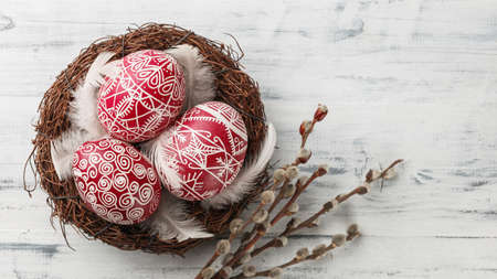 Pysanky, decorated Easter eggs in the nest, pussy willow branches and feathers on white wooden...