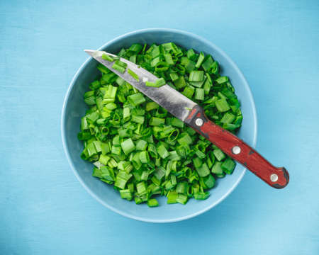 Sliced, chopped spring, salad, green onions or scallions with sour cream in a bowl on the blue backgroundの写真素材