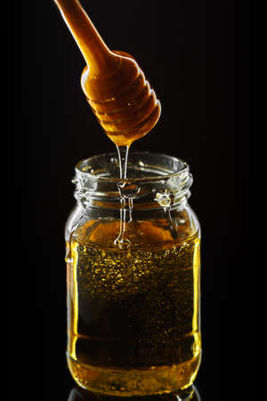 Honey jar with dipper and flowing honey on the black backgroundの写真素材