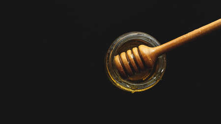 Honey jar with dipper on the black background. Toned image with copy space for your text