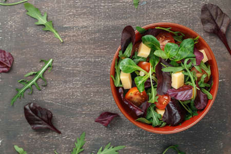 Fresh spring vegetable salad with tomatoes, cheese and leaves mix of rucola, frisee, radicchio and lamb's lettuce on wooden backgroundの写真素材