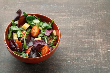 Fresh spring vegetable salad with tomatoes, cheese and leaves mix of rucola, frisee, radicchio and lamb's lettuce on wooden backgroundの写真素材