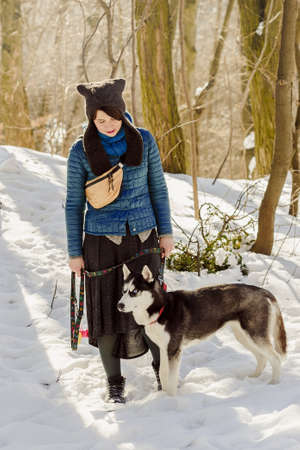 Stylish woman wearing funny hat walking in the park with her Siberian husky dog on a leashの写真素材