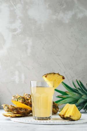 Pineapple freshly squeezed juice in glass on a wooden table over grey concrete background, front viewの写真素材