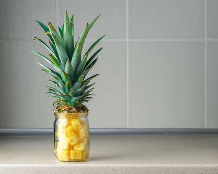 Fresh juicy pineapple pieces in a glass jar on the kitchen table against grey rile backgroundの写真素材