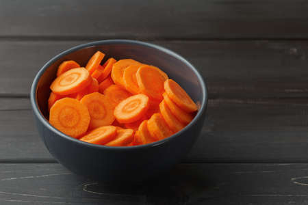 Sliced carrots in a bowl on black wooden background