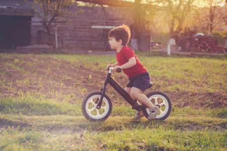 Little boy rides a balance bike in the countryside at sunset. Run bicycle without pedalsの写真素材