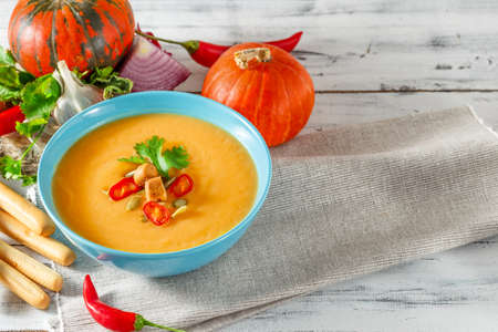 Pumpkin soup with chili pepper, pumpkin seeds, croutons and parsley in blue bowl on white wooden backgroundの写真素材