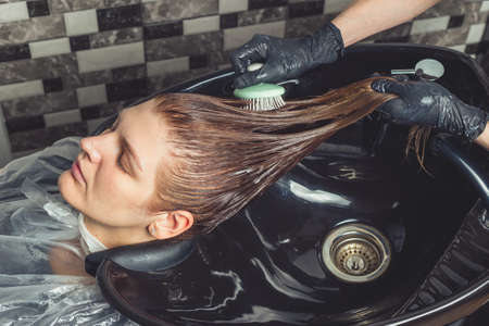 Haircare procedure in beauty salon. Hairdresser is brushing woman's hair spreading a treatment mask or conditionerの写真素材