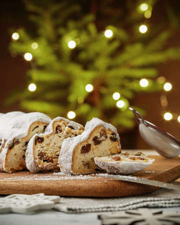 Stollen, traditional German Christmas yeast cake with raisins on the table, fir tree lights bokeh on the backgroundの写真素材