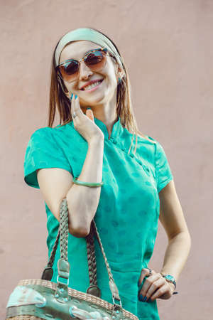 Outdoor portrait of a young beautiful fashionable cheerful lady wearing green dress posing on a street of the old city. Female fashion. City lifestyleの写真素材