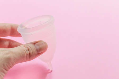 Close up of woman hand holding menstrual cup over pink background. Women health concept, zero waste alternativesの写真素材