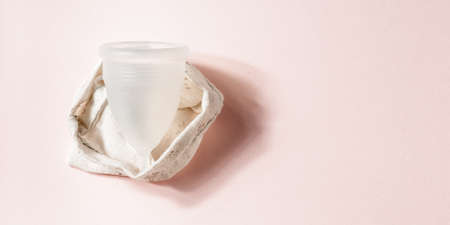 Menstrual cup in cotton bag on pink background. Alternative environmentally friendly feminine...