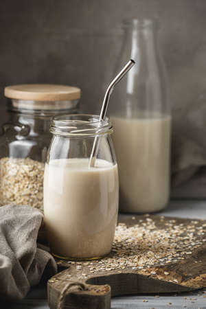 Non dairy oat milk in glass jar with metal reusable drinking straw on rustic background. Oat flakes scattered on the table.の写真素材