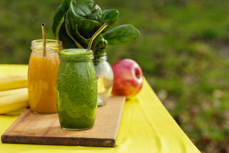 Fruit smoothies in the glass jars on yellow table with green blurred garden as background. Healthy...