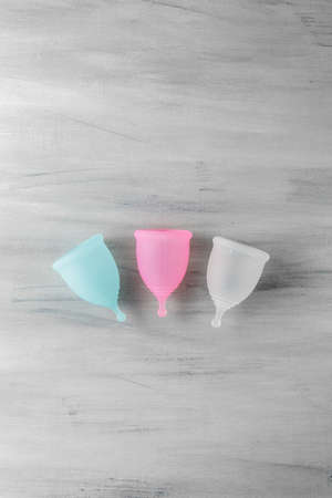 Three colorful menstrual cups on grey wooden background. Alternative method of bleeding protection during the period. Women health conceptの写真素材