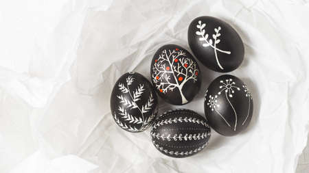 Pysanky on the white crumpled paper background. Easter eggs decorated with wax-resist dyeing technique, traditional for Eastern European countries, wide format, top view, copy spaceの写真素材