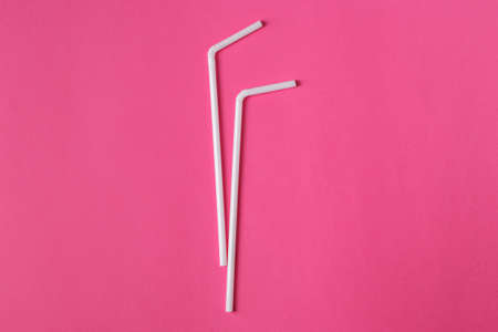Two white plastic straws on pink background. Plastic pollution. Environmental concept