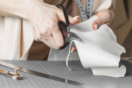 Female handbag designer measuring leather and cutting out details in a workshop studio