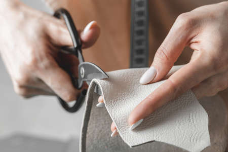 Female handbag designer measuring leather and cutting out details in a workshop studio