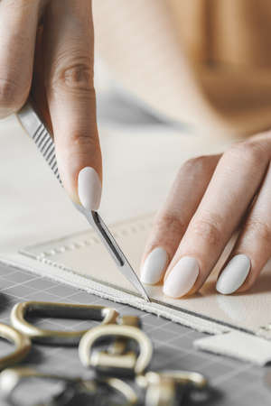 Female handbag designer measuring leather and cutting out details in a workshop studioの写真素材