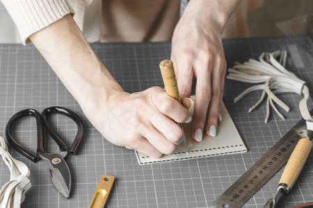 Female handbag designer measuring and cutting leather in a workshop