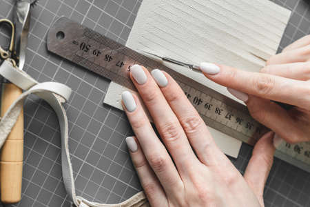 Female craftswoman measuring and cutting white leather fringe for boho style handbag detailsの写真素材
